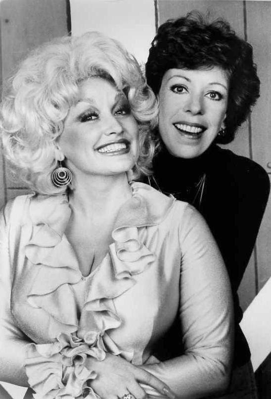 Black-and-white photo of two women smiling closely together, one seated and the other standing behind her with arms around her.