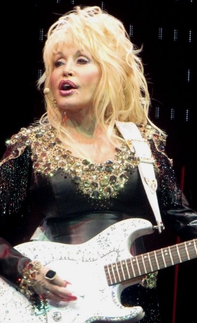 A performer on stage playing a white electric guitar under stage lighting.