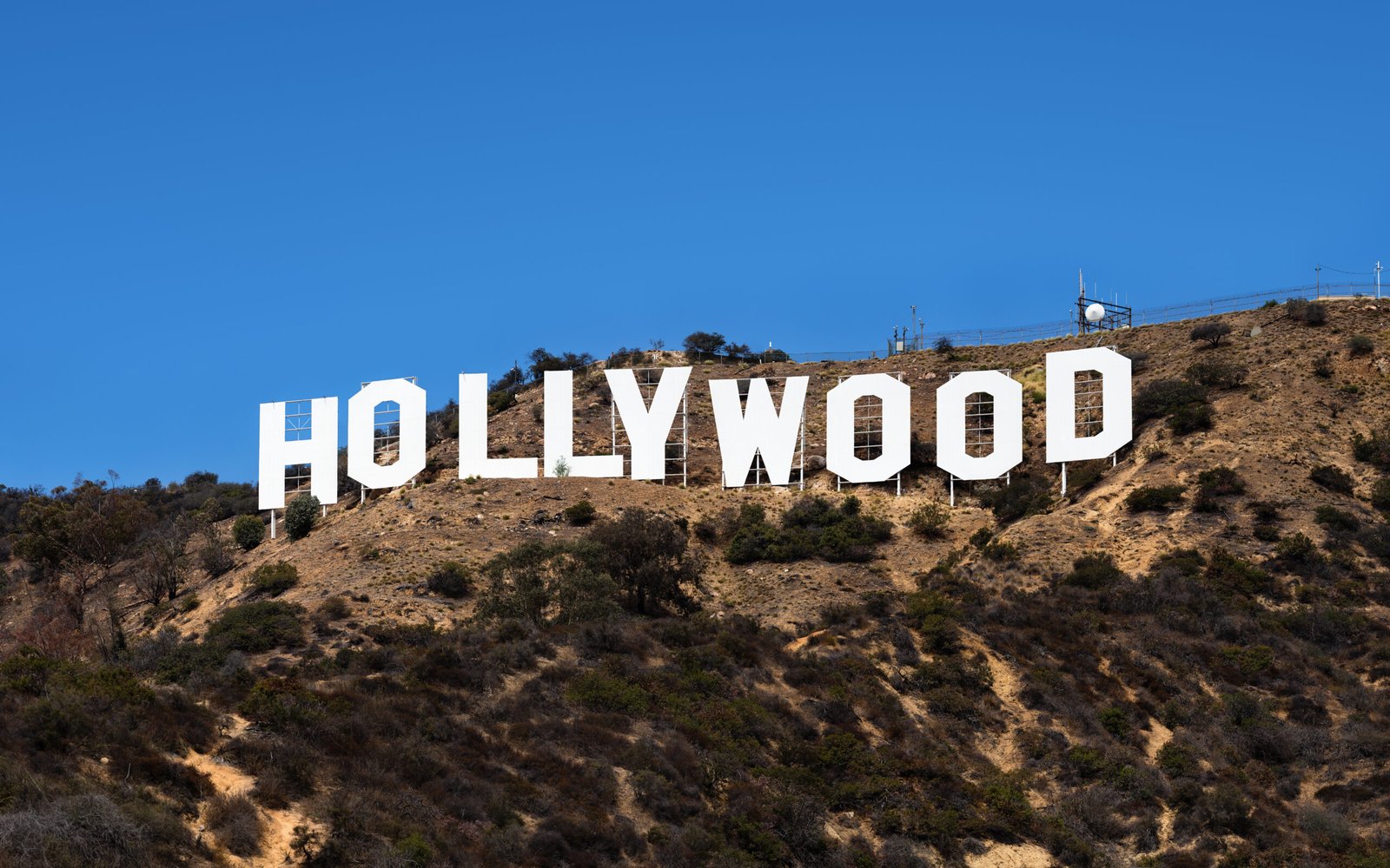Large white letters spelling “HOLLYWOOD” mounted on a dry hillside above Los Angeles beneath a clear blue sky.