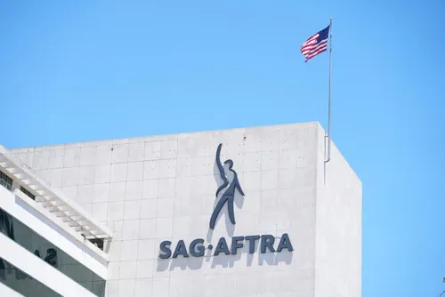 Building exterior with large SAG-AFTRA logo on the wall and an American flag flying on a flagpole above against a clear blue sky.